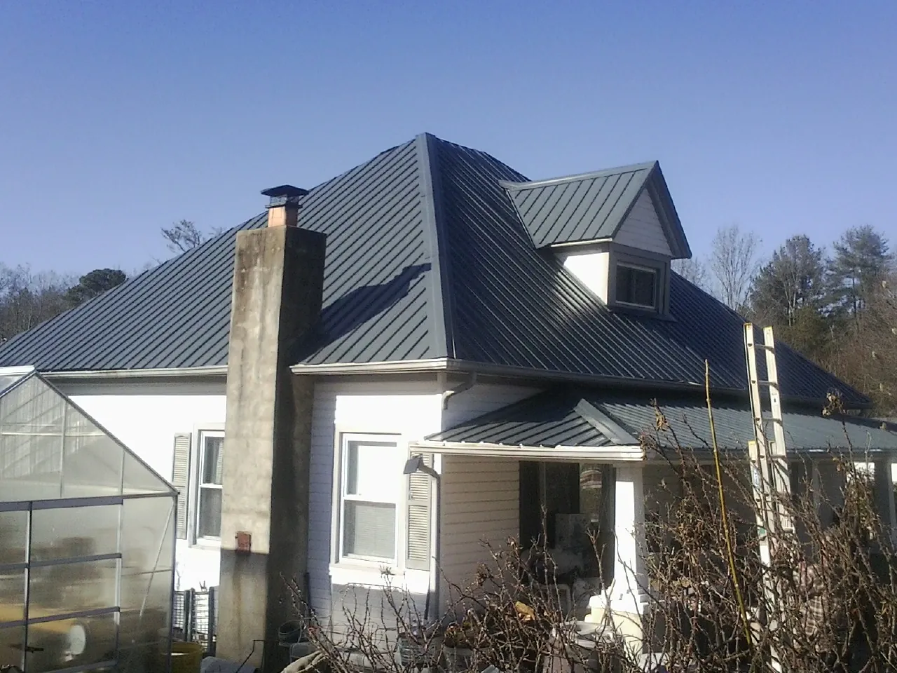 Dark blue standing seam metal roof on a white farmhouse with dormer — Slate & Tile Roof Repair by Roofing Brothers in Bladenboro