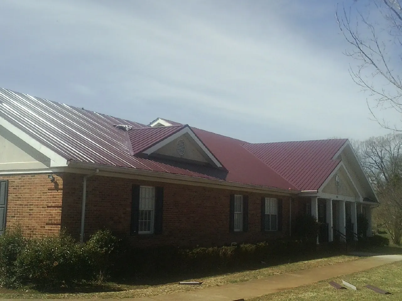 Red metal roof with gabled entries on a long brick building, from a Hail Damage Roof Repair job in Bladenboro