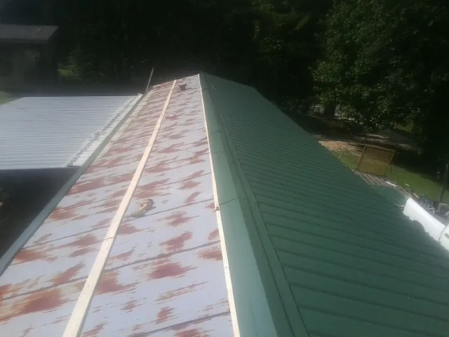 Old rusted panels beside newly installed green metal roofing — Wind Damage Roof Repair by Roofing Brothers in Bladenboro