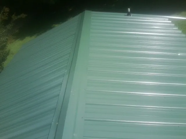 New green metal panels meeting at the ridge of a roof — Flat Roof Repair work by our crew in Bladenboro