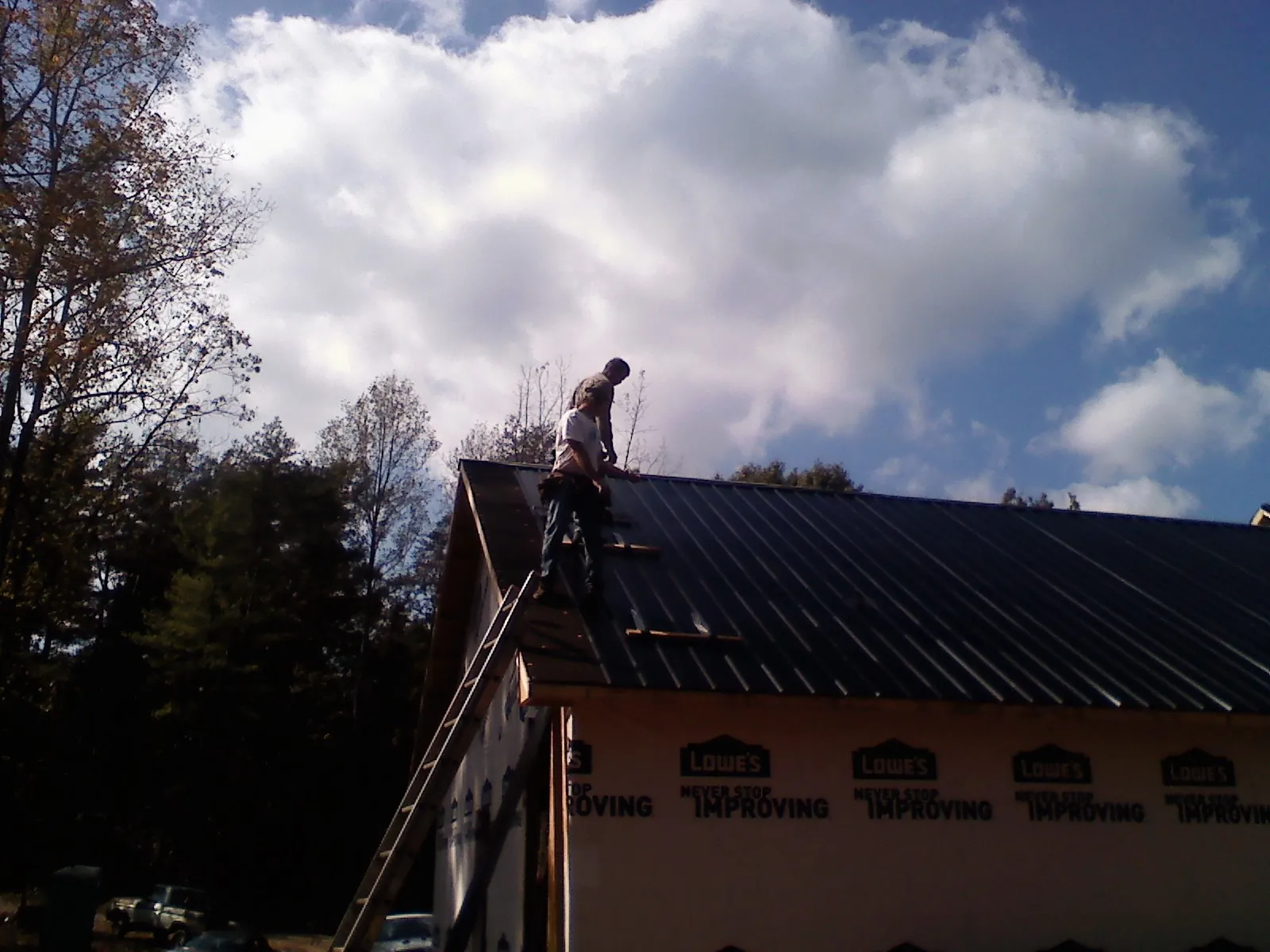 Roofer fastening dark metal panels high against a cloudy sky, from a Roof Inspection job in Bladenboro