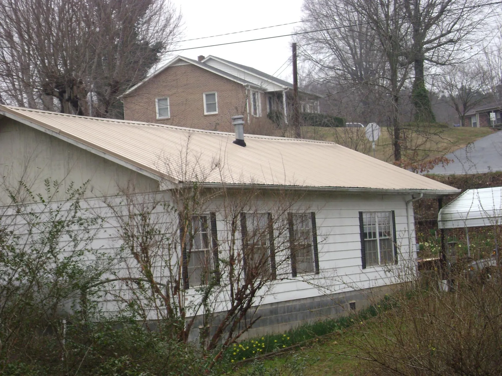 Tan metal roof on a white sided house set into a hillside — Commercial Roofing by Roofing Brothers in Bladenboro