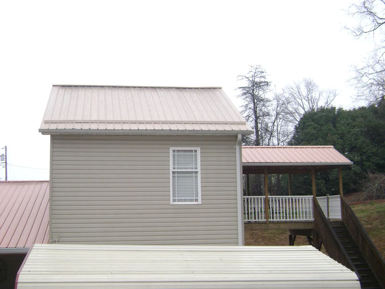 Tan metal roofs on a two story addition and attached porch, from a Roof Replacement job in Bladenboro
